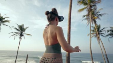 VR kulaklıklı kadın tropikal plajı keşfediyor, artırılmış gerçeklik oyunuyla etkileşime geçiyor, doğadaki el kol hareketi, büyüleyici teknoloji deneyimi, güneşli egzotik bölgelerde okyanus esintisini hissediyor..