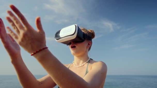 シミュレーションされた環境と相互作用するデジタル海辺の風景の女性アバター Vrヘッドセットの女性は 手でジェスチャーしてバーチャルビーチシーンを探索します Vrトラベル 海によるレジャー活動 — ストック動画
