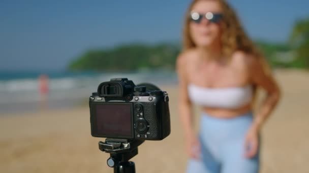 内容创建者表演 记录追随者的时髦举动 穿着管状上衣和牛仔裤片的女人带着相机在海滩上跳舞 艳阳天 海景背景 社交媒体聚焦 — 图库视频影像