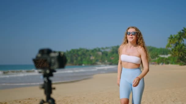 ソーシャルメディアコンテンツクリエイター映画トレンディなダンスルーチン 女性のスタイリッシュな衣装は砂浜でリズム的なダンスの動きを実行します カメラは活気のある振り付けを記録します 晴れた海岸の背景 — ストック動画