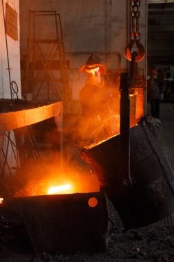 Endüstriyel dökümhane, vitrin üretim süreci. Koruyucu ekipman işçisi çelik fabrikasına erimiş metal döküyor. Metal işçisinin güvenlik ekipmanlarında yüksek sıcaklıkta metalürjik prosedürü.