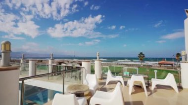 İdeal gayrimenkul, tatil kirası, otel tanıtımı. Sahile bakan lüks mülkler havuz, teras, modern sandalyeler, panoramik deniz manzarası.
