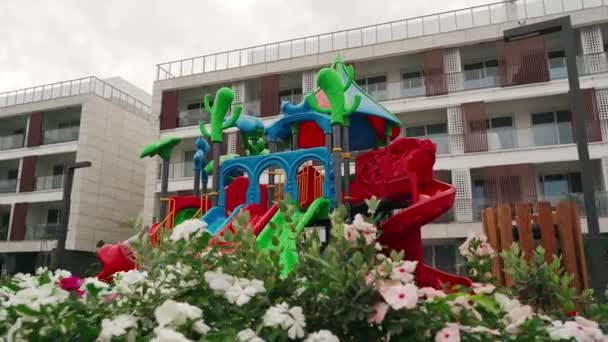 Colorful Playground Equipment Stands Blooming Flowers Modern Apartment Buildings Background — Stock Video