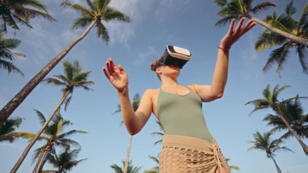 伸出双臂 她在棕榈树之间体验到了更大的真实感 在模拟的热带环境中体现了一个数字化身 女性在户外使用Vr耳机 沉浸在虚拟模拟中 — 图库视频影像