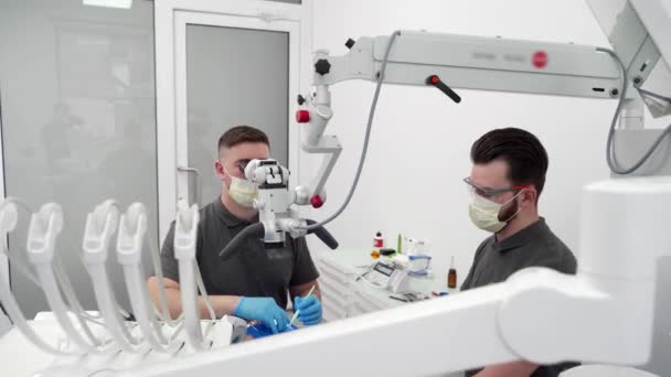 現代歯科クリニックで顕微鏡を使用したアシスタント手術患者歯科医 口腔外科医は根管を浄化し 歯科神経を刺激する エンド歯科治療患者ルートカナル — ストック動画