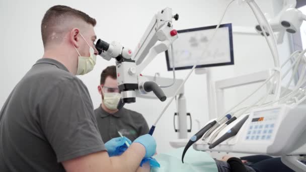 在现代牙科诊所使用显微镜对男牙进行辅助手术 口腔外科医生清理根管并烧灼牙神经 牙科医生治疗患者根管狭窄 — 图库视频影像