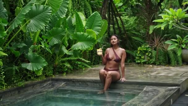 随意的闲暇 在异国情调中宁静的氛围 双族女人在丛林游泳池边放松 享受热带鸡尾酒 比基尼装束 美味佳肴 思量和平的天性 体现了夏天的奢华 Slomo — 图库视频影像