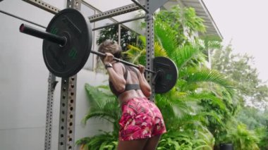 Fitness ekipmanlarıyla güçlü eğitim egzersizleri. Çift ırklı kadın, zengin spor salonunda halter çömelmesi yapıyor. Atletik kadın, spor giyim, vücut tonuna odaklan. Sağlık, sağlık rutini. Yavaşla