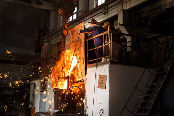 Worker manages molten metal pouring in industrial environment, steel production high-temperature furnace, sparks flying, metallurgy expert oversees smelting process foundry scene protective gear.
