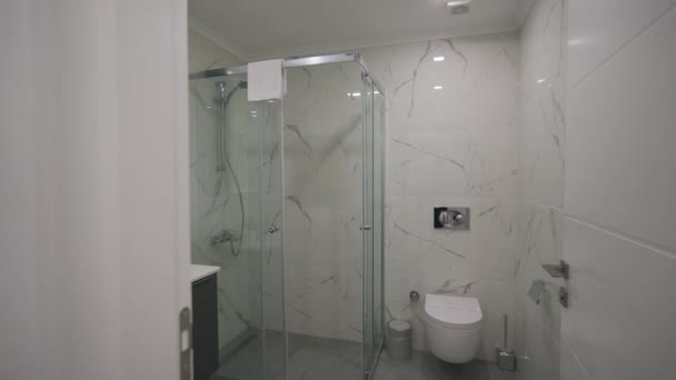 モダンなバスルームのインテリアは ウォークインシャワー 光沢のある大理石の壁 洗練された白い据え付け品がアップスケールの都市アパートで虚栄心を映し出しています — ストック動画