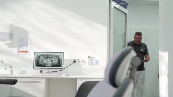 現代歯科オフィス スクリーンのパノラマの歯科X線 男性の歯科医と女性の患者が入ってきて 座っています 医師は患者に相談する スクリーン上のX線の歯を女性に説明する Orthodontist — ストック動画
