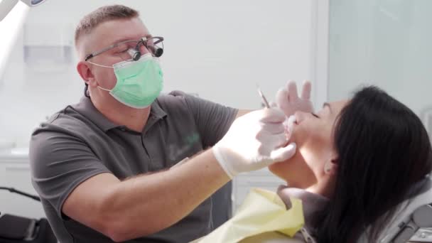 ジルコニアのベニヤおよび王冠を取付けるために女性の患者歯を準備する歯科双眼鏡の男性歯科医 マスクに集中した症候学者は 患者の猫を扱います 仕事中のドクター クローズアップ — ストック動画