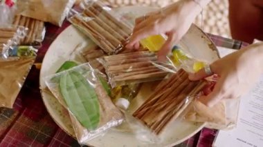 Ziyaretçi araştırıyor, aromatik hediyeler seçiyor, hareketli pazarın ortasında yerel zanaatı keşfediyor. Eller markette seramik tabakta tarçın çubukları ve yaprak paketleri düzenler.