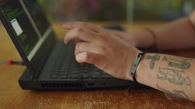 Ekrandaki odaklanma kodunda, dövmeli eller daktilo ediyor. Programcı dizüstü bilgisayarda kod yazar, parmakları hızla tuşlara basar. Web geliştirme, siber uzay iş akışı. Yavaş çekim.