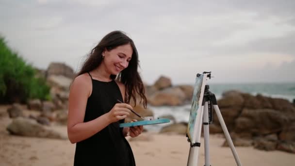 바람이 머리카락 창조적 분위기를 드레스를 예술가는 해안의 캔버스에 황혼에 바다를 — 비디오