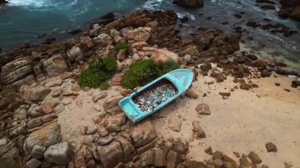 無視された廃棄物は船を巻き込み 岩に囲まれた オーバーヘッドビューは 海洋および沿岸汚染の深刻な問題を示す プラスチック容器で詰め込まれた座礁した 再利用されたボートをキャプチャします — ストック動画