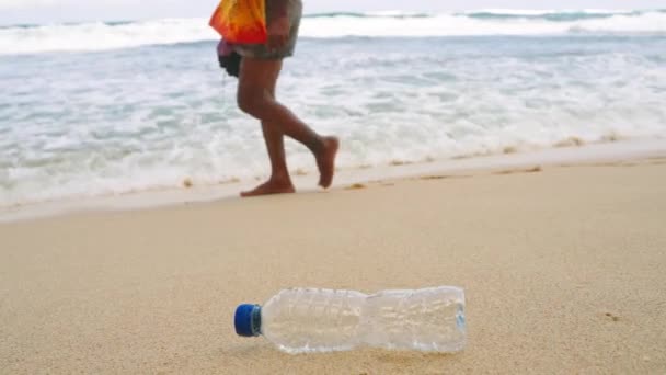 汚染問題は 人々がゴミを無視して過ぎ去ったように明らかであり 海洋のエコの懸念を強調しています 捨てられたプラスチック製のボトルは砂浜にあり 近くに波が衝突しています クリーンアップの取り組みが必要 — ストック動画