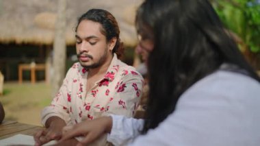 Gay BIPOC grubu fresk yemeğinin tadını çıkarıyor. Çeşitli arkadaşlar güneşli açık kafede menüye bakarlar. Seçenekler tartışıldıkça sohbet de devam eder. Gelişigüzel, kapsayıcı bir toplantı..