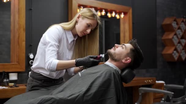 女性は クリッパー トリムひげ 髪を使用して トレンディな外観を作成します プロの床屋は現代サロンで男性の顧客にスタイリッシュなヘアカットを与えます グルーミングセッション サロンインテリア 進行中のヘアカット — ストック動画