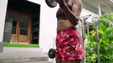Formda bir kadın, spor salonunda halterlerle biseps yapıyor. Tropikal olarak vücut şekillendirme bina egzersizlerine odaklanıyor. Aktif yaşam tarzı şık spor kıyafetleri, yavaş çekim fitness..