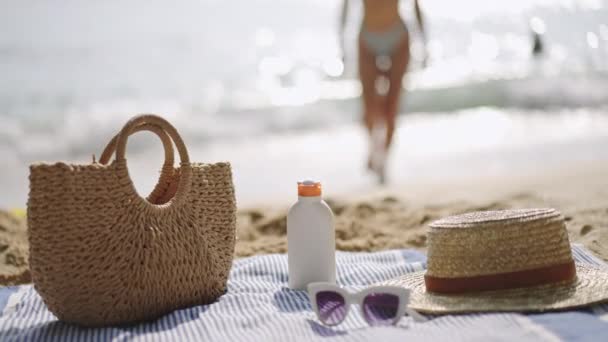 人は海に向かって歩き 日光浴の準備をする ビーチの必需品はタオル 日焼け止めのびん 紫外線保護に置きました カジュアルな夏のアクセサリー 色合い 砂浜のトート スローモーション — ストック動画