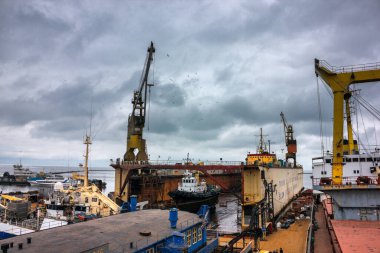 Römorkörler deniz operasyonlarına yardım ediyor, ağır vinçler araç gereçleri kaldırıyor. Yüzen rıhtımı olan bir sanayi gemisi, bakım yapılan gemiler. Denizcilik işyeri ve taşımacılık endüstrisi üzerinde bulutlu bir hava