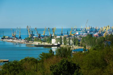 Gemiler limana yanaştı, mavi deniz arka planında. Sahil endüstriyel liman, kargo vinçleri ufuk çizgisine hakim. Ticaret merkezi, deniz taşımacılığı, küresel lojistik konsepti. Ağaç kaplı liman, nakliyeyle meşgul..