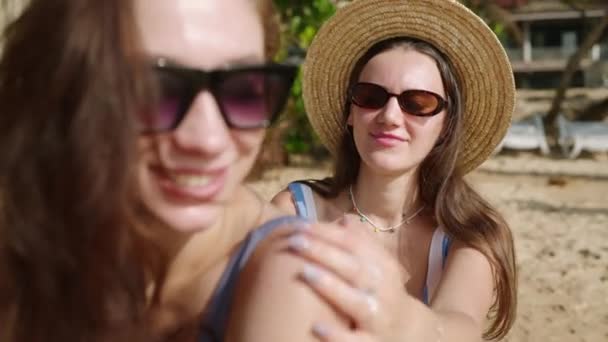 在沙滩上给女人涂防晒霜的女孩 微笑的女士准备在海滨晒日光浴 把防晒霜涂在皮肤上 日光浴保护皮肤的度假概念 — 图库视频影像
