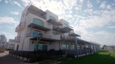 Birden fazla balkonlu deniz manzaralı villa manzaralı deniz kenarında yaşam, yeşil çimenlik, lüks gayrimenkul yatırımı, güneşli bir gün.