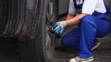 Profesyonel, araba tekerindeki fındıkları sıkıyor. Mavi üniformalı oto tamircisi, benzin istasyonunda tork anahtarı kullanarak lastik kuruyor. Araç bakımı, otomotiv endüstrisinde doğruluk.