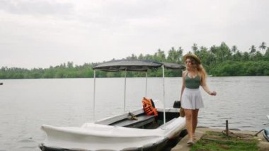 Gündelik kıyafetlerle tek başına gezen sakin suda tekneden çıkar. Macera arayan kadın nehir teknesinden iniyor, tropik kıyılara ayak basıyor, yemyeşil bir çevreyi keşfetmeye hazırlanıyor. Yavaş çekim.