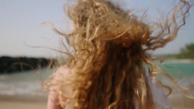 Rüzgarda savrulan sağlıklı uzun saçlar. Oldukça kıvırcık, havadar, güçlü saçlı, sahilde poz veren, deniz sörfü yapan bir model. Doğal, parlak saçlı beyaz bir kadın okyanus kıyısında güneşli bir günün tadını çıkarıyor. Yakın plan..