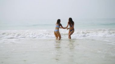 Mayo giymiş neşeli, ıslak kızlar dalga dalga deniz sörfü yapıyor. Çekici bayan arkadaşlar okyanusta birbirlerine su sıçratma oyunu oynarlar. Deniz köpüklü dalgalardan hoşlanan formda genç kadınlar. Yavaş çekim.