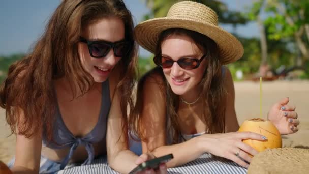 快乐的女孩躺在阳光下 在热带海滩用手机浏览社交媒体 穿着比基尼笑着的女人晒黑了 在海滨冲浪 暑假时打电话成瘾的年轻女性的闲暇时间 — 图库视频影像