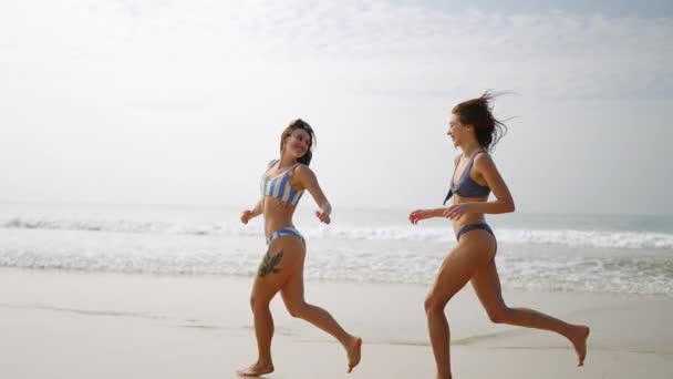 Dvě Šťastné Dívky Bikinách Běhající Vlnách Mořské Vody Veselé Kamarádky — Stock video