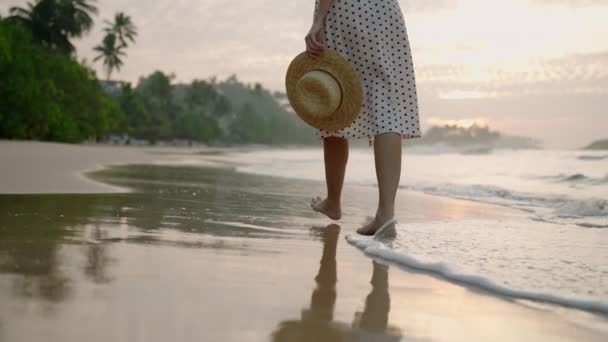 海のサーフウォーターエッジで裸足で日没する女性の足 泡立った水を散らす 若い女性の足は夏の夕方に海岸沿いにゆっくりと歩いています 海辺で休暇を楽しむドレスの女性 — ストック動画