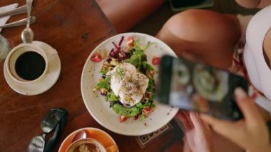 Avokado tostu, haşlanmış yumurta, kahve ve hippi kafeteryasında kapuçino ile fotoğraf çeken kadın eller. Lokantada masada kahve ile sağlıklı bir tost. Kahvaltıda lezzetli bruschetta..