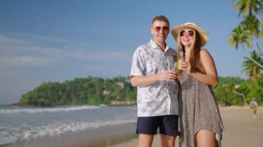 Romantik çift, tropikal seyahatte bir kadın güneşli sahil sahilinde elinde limonata şişeleriyle kameraya bakar, klink, chat, kahkaha. Neşeli beyaz erkek, randevuda dişi deniz kıyısında içkinin tadını çıkar..