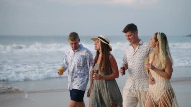 Erkek arkadaş grubu, taze meyve suyu şişeli kadınlar güneşli tropik plajlarda yürüyor, içiyor, konuşuyor, gülümsüyor. İki neşeli Kafkas çifti, deniz kıyısında eğlenip, içeceklerin tadını çıkarın. Yaz tatili