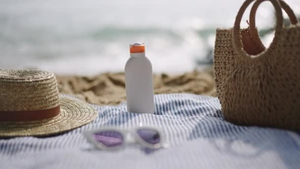 背景中的海浪 休闲的概念 夏天的皮肤护理 海滩用具布置在沙滩上 防晒霜在编织的帽子 窗帘和带条纹的毛巾上 慢动作 — 图库视频影像