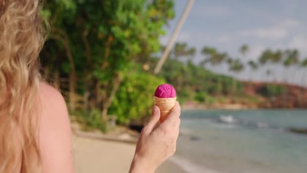 女人悠闲地在沙滩上漫步 手中拿着新鲜的冰淇淋 享受着平静的海滨漫步 棕榈树飘扬 体现着轻松的夏天氛围 慢动作 — 图库视频影像