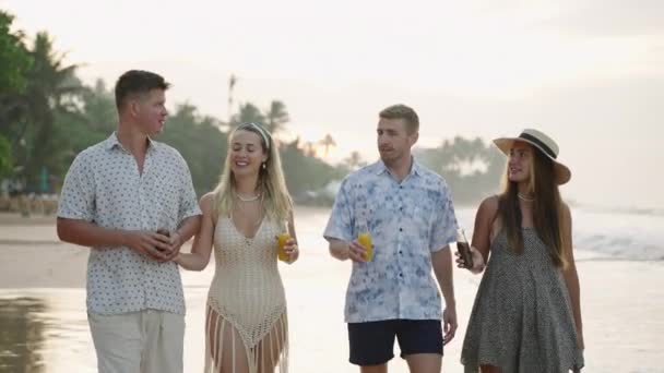 朋友们 男人们 女人们带着新鲜的果汁瓶在阳光灿烂的热带海滩上散步 两只快乐的高加索夫妇在海滨享受着饮料和寒冷 — 图库视频影像