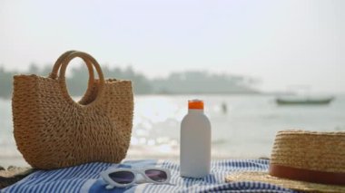 Güneş gözlüğü, güneş kremi şişesi, hasır şapka, deniz kıyısında botlarla örülmüş çanta. Plaj esasları, yaz güneşinden korunmak için çizgili havluya serilmişti. Ultraviyole savunma için tatil aksesuarları.