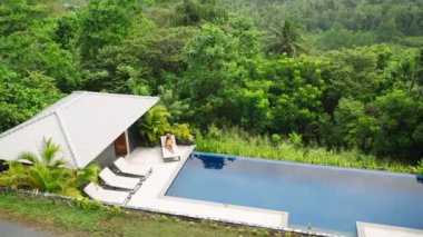 Mayo salonlarında sonsuzluk havuzunda bir kadın, yeşil orman arkaplanı huzurlu bir tatil havası yaratır. Tropikal ortamda lüks havuzda rahatlayan bir kadının genel çekimi. Kaçış, lüks seyahat. Yavaşla