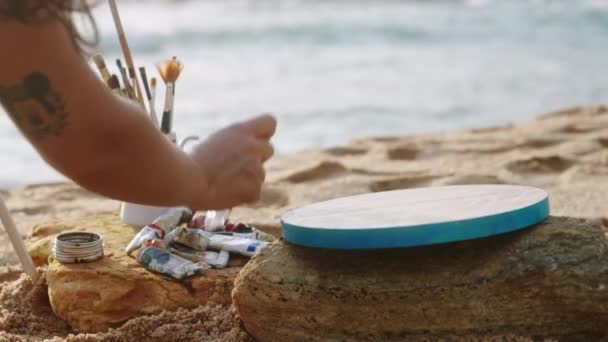 海浪附近沙滩上的创意设置 女画家在日落时在海边准备彩色调色板作画 双手混合颜料 安排刷子在海滩上准备艺术项目 慢动作 — 图库视频影像