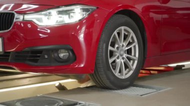 Asansörde kırmızı sedan, garajda bakım, modern diyaj aletleri, güvenlik kontrolü. Otomatik servis teknisyeni araba atölyesindeki hidrolik oyun dedektörü ekipmanlarını kullanarak araç süspansiyonunu, direksiyon sistemini denetliyor.