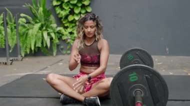 Atletik, kaslı fiziği sağlıklı ağırlık yönetimi ile sergileniyor. Formda bir kadın açık spor salonunda halter egzersizi yaptıktan sonra rahatlar, meditasyon pozu verir. Kentsel fitness seti, dışarıdaki kişisel sağlık hedefleri. Yavaşla