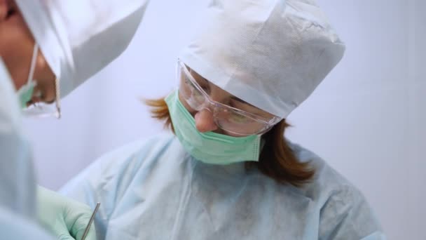 保護眼鏡の歯科女性アシスタント フェイスマスクは現代の医療オフィスで患者と協力しています インプラント手術中に口腔外科医を支援する看護師 歯科インプラント手術 クローズアップ — ストック動画
