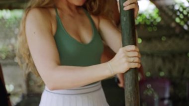 Geleneksel baharat hazırlama tanıtımı, organik malzemeden aroma. Yeşil bluzlu, beyaz etekli, tarçın kabuklu bir kadın. Katılımcı, yeşillikler arasında aktif kültürel deneyimden hoşlanıyor.