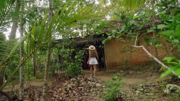 探险探险者冒险进入热带植物区系中的乡村避风港 戴帽子的女人探索废弃的丛林小屋 好奇心导致荒废的房屋从荒原走向荒废的房屋 — 图库视频影像